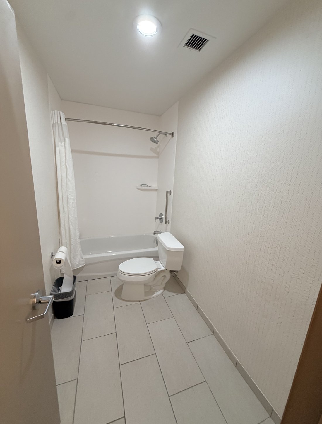 The original bathroom before redesign — white walls, white tile, standard tub and shower curtain