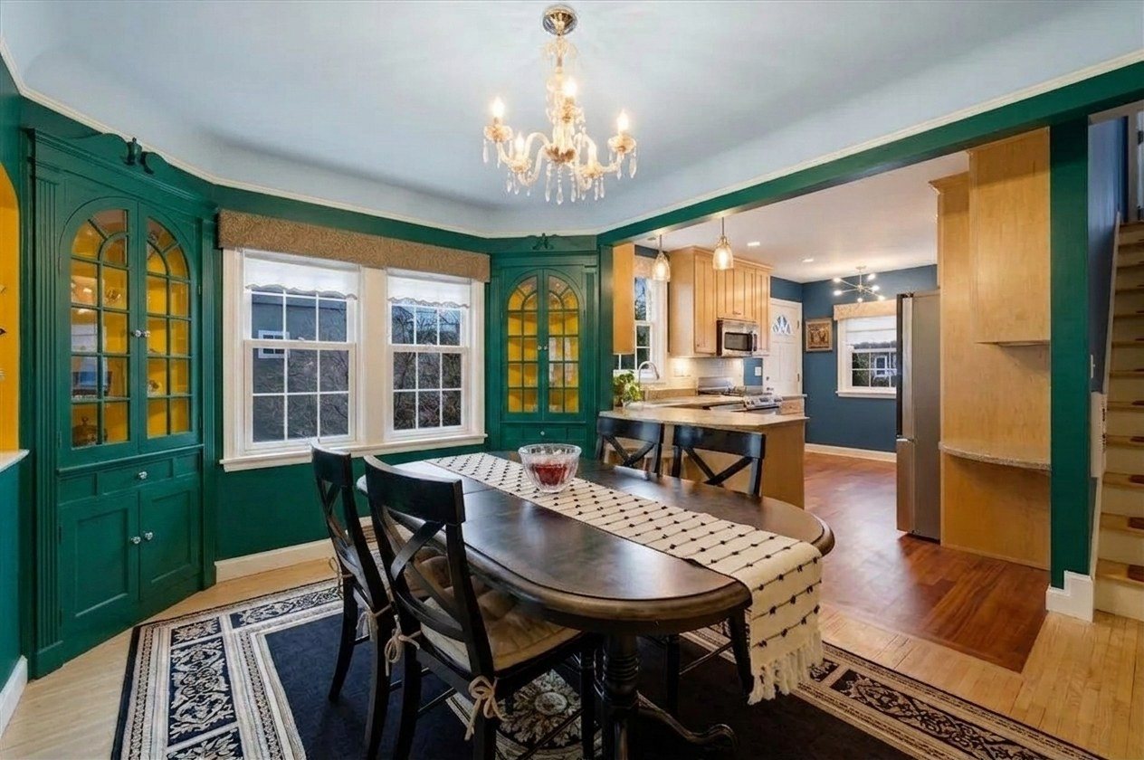A dining room in the Emerald Harbor color story, deep green walls with gold behind the cabinet glass and a pale sky ceiling